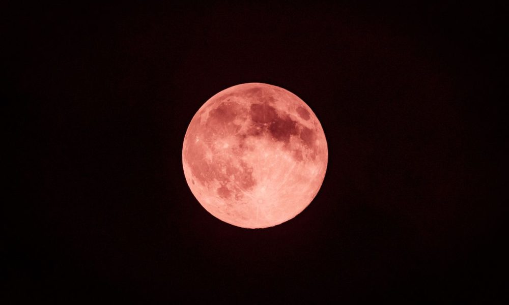 Bulan purnama kemerahan bersinar di langit gelap, ilustrasi Strawberry Moon 2025.