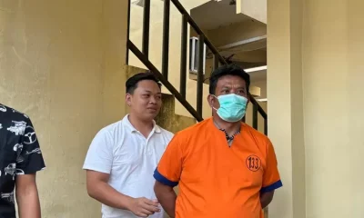 Ayah Farel Prayoga berbaju tahanan oranye bermasker digiring petugas di area tangga kantor polisi Banyuwangi.