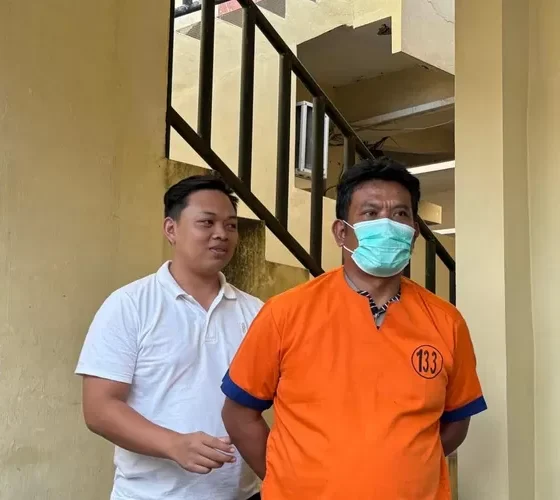 Ayah Farel Prayoga berbaju tahanan oranye bermasker digiring petugas di area tangga kantor polisi Banyuwangi.