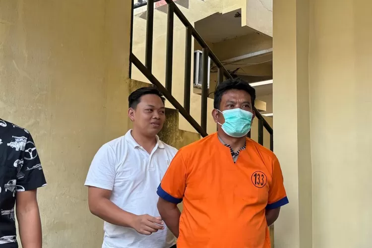 Ayah Farel Prayoga berbaju tahanan oranye bermasker digiring petugas di area tangga kantor polisi Banyuwangi.