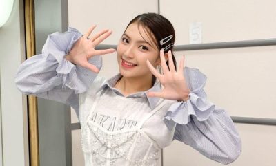 Gracia JKT48 tersenyum cerah sambil berpose tangan membentuk angka sepuluh di belakang panggung.