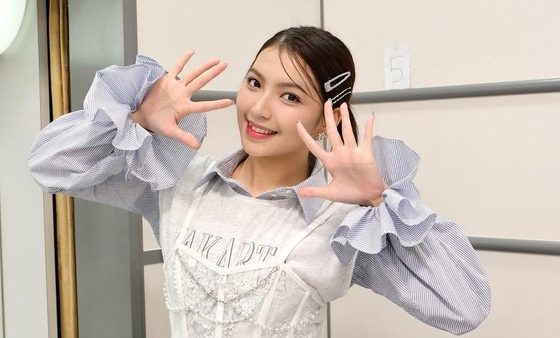 Gracia JKT48 tersenyum cerah sambil berpose tangan membentuk angka sepuluh di belakang panggung.